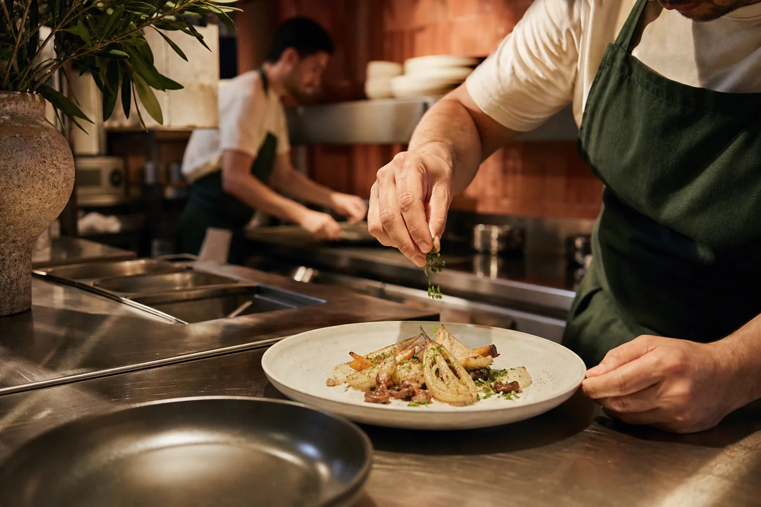 Un cocinero termina un plato en el pase de una cocina mediterránea